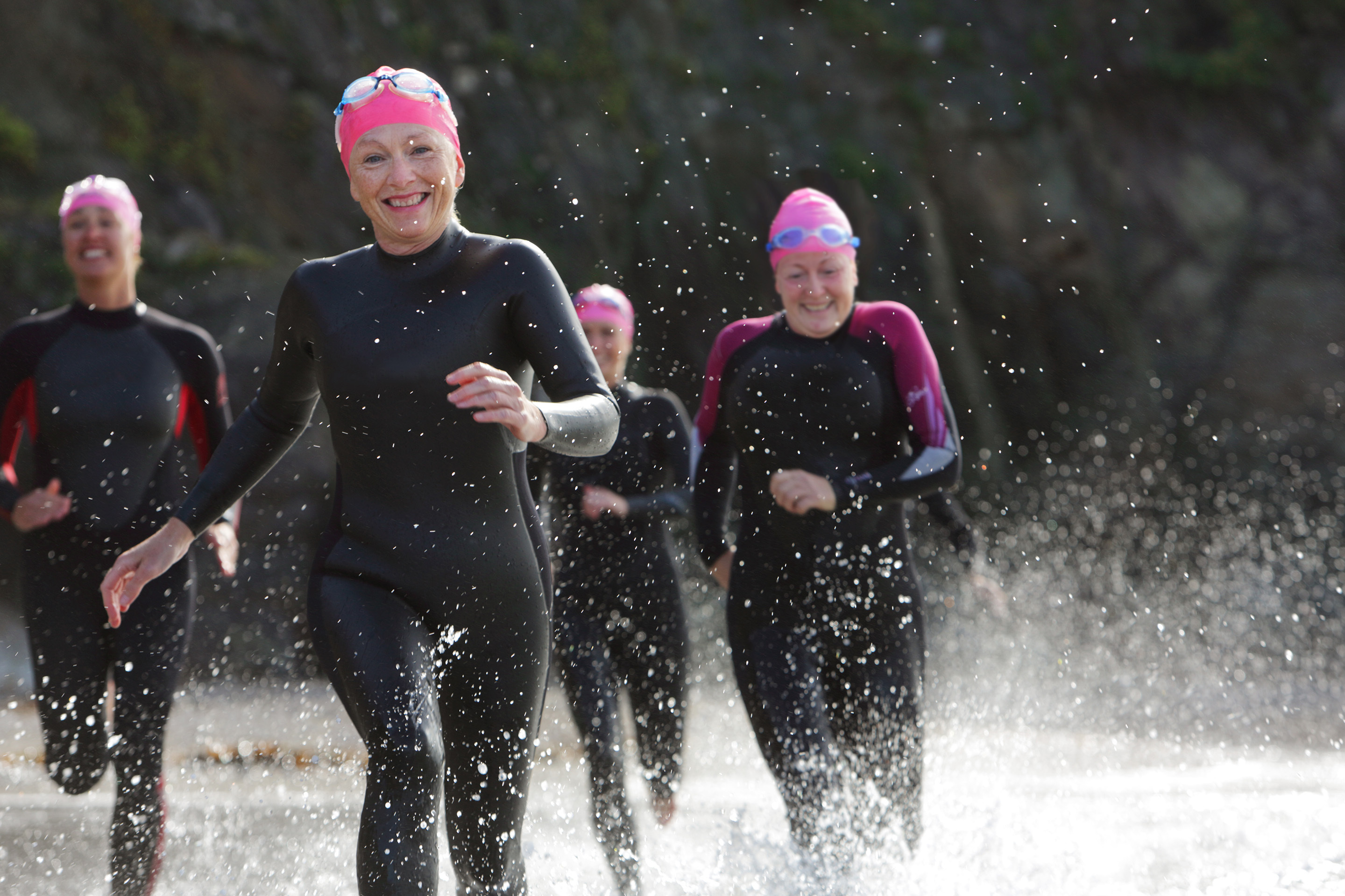 Group of women in wetsuits running in the sea