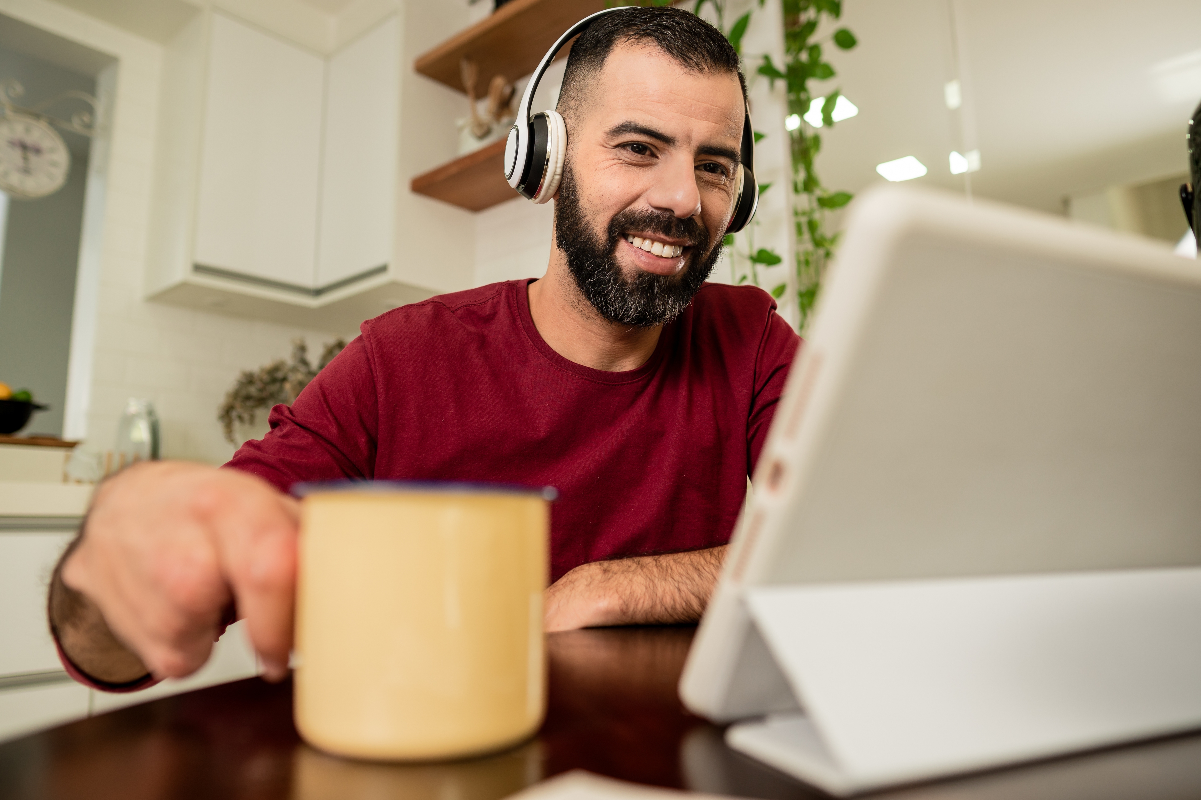 Man with his laptop wearing headphones drinking out of a mug