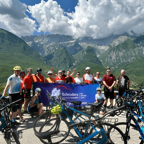 Group of cyclists at the top of a mountain holding a banner