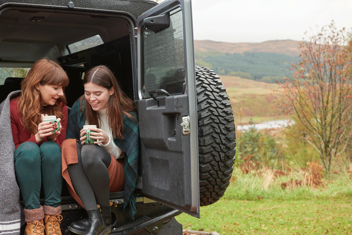 Two women sitting in the back of a car drinking hot drinks