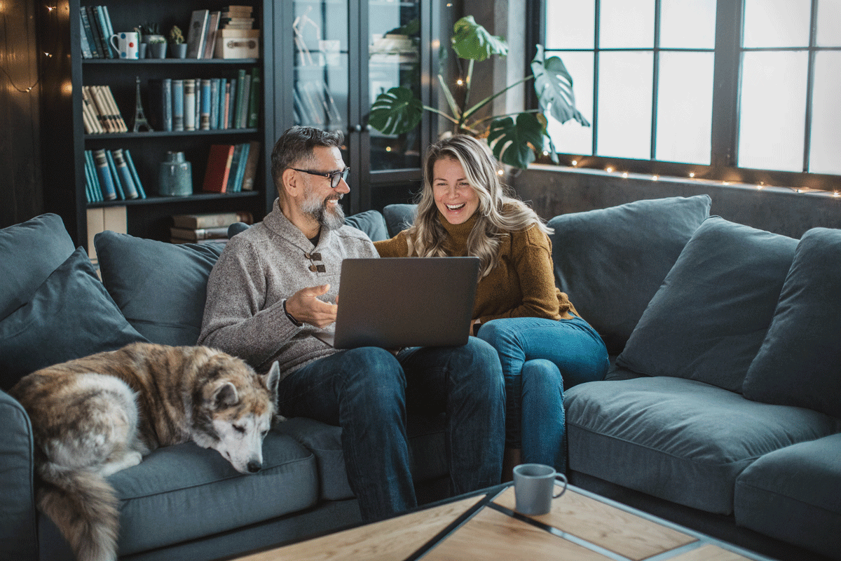 Man and women sitting on the sofa with their dog looking at the laptop